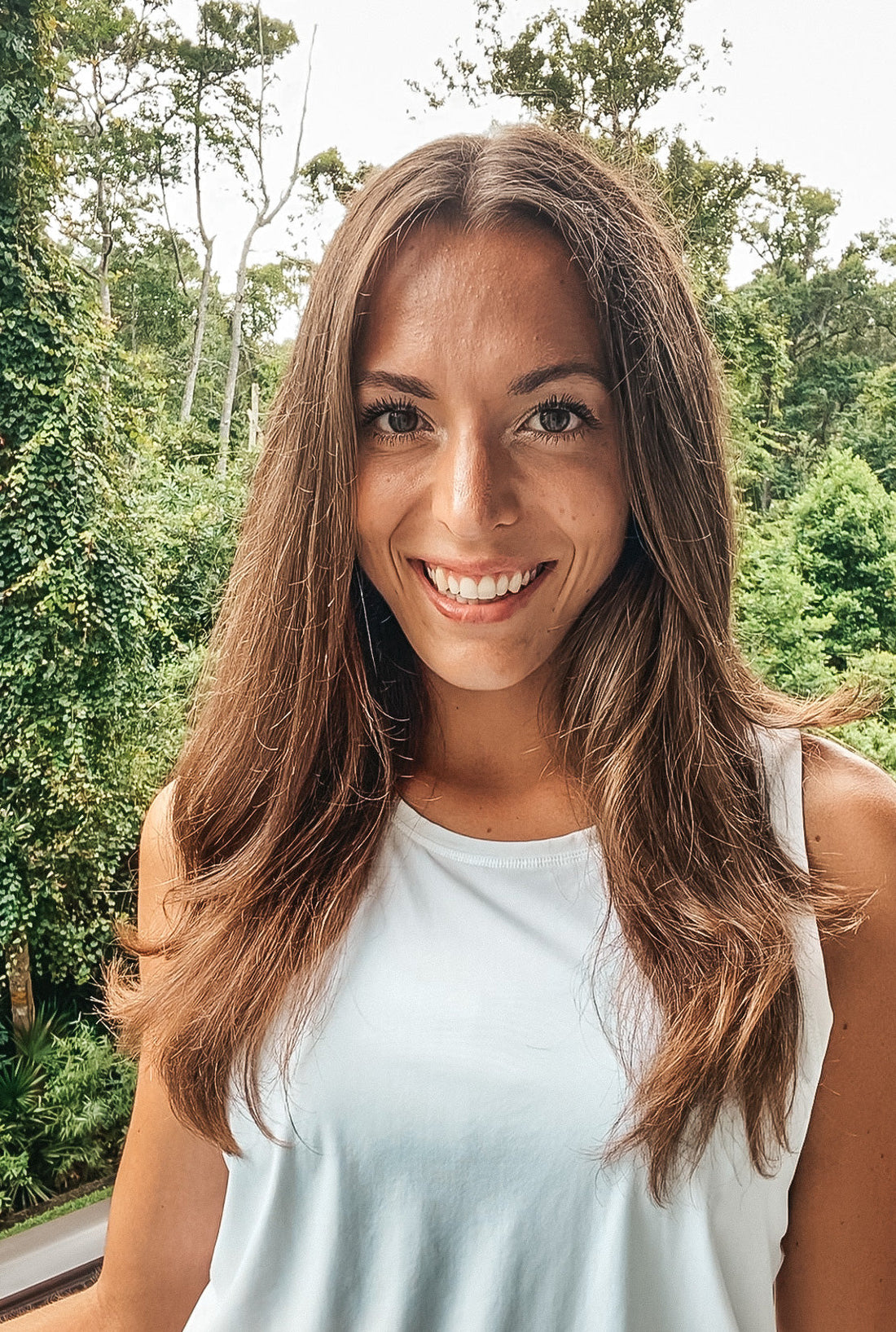 Founder of Inspira Tlb smiling with white tank top on and greenery behind her.
