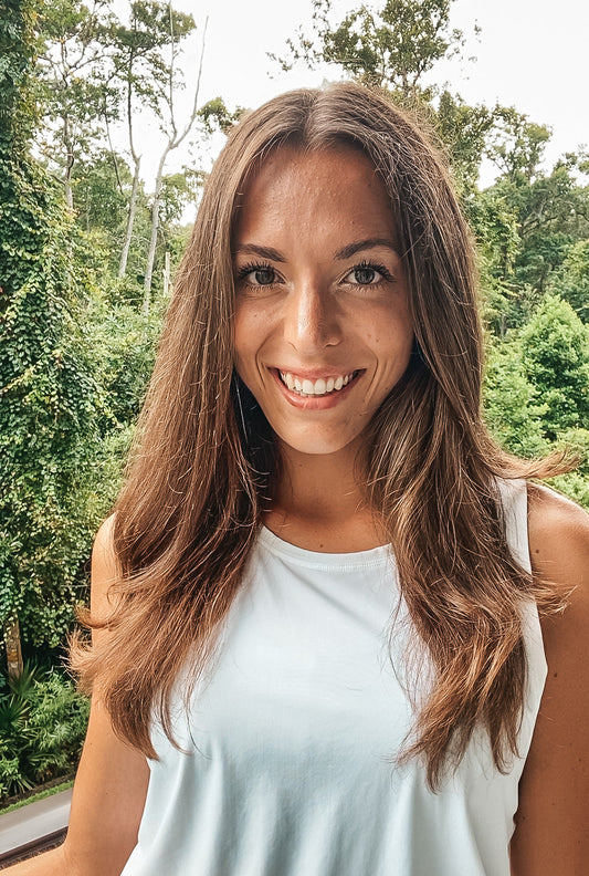 Founder of Inspira Tlb smiling with white tank top on and greenery behind her.